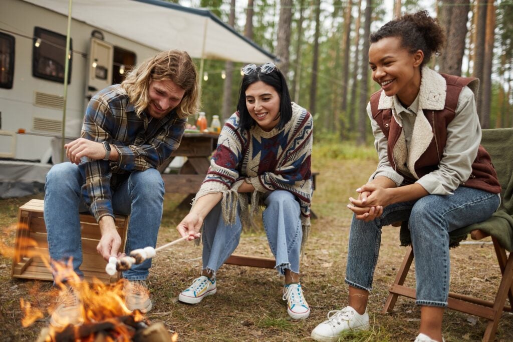 A group of friends roast marshmallows at a RV camp site.