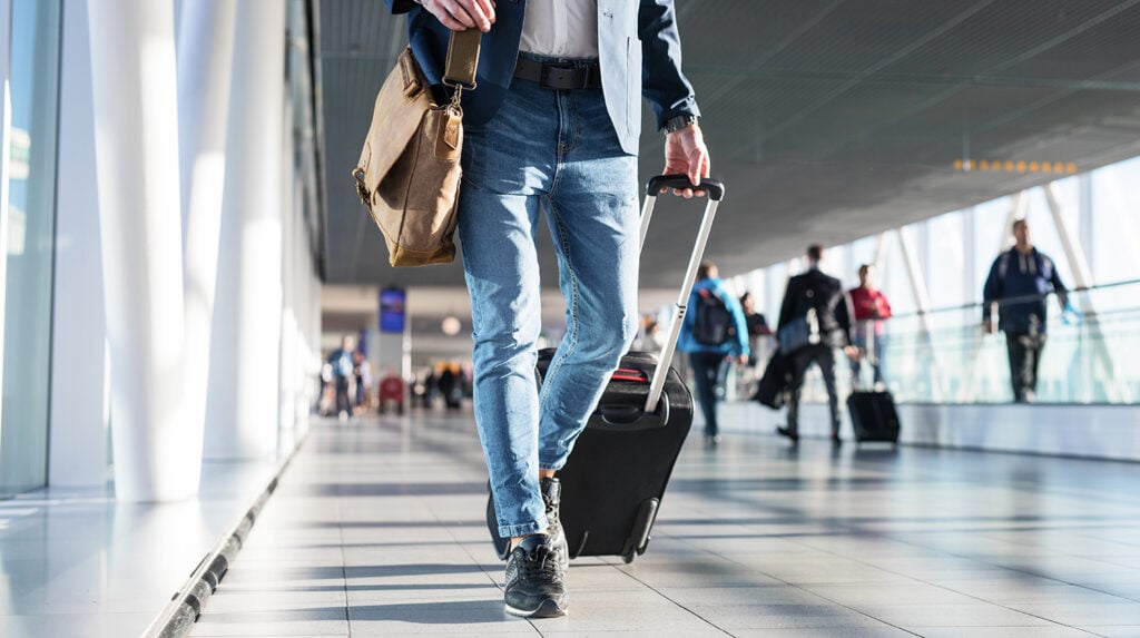 Man with shoulder bag and hand luggage walking in airport terminal