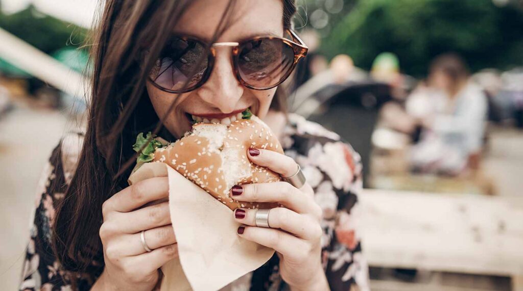 Young woman wearing sunglasses enjoys a burger outdoors
