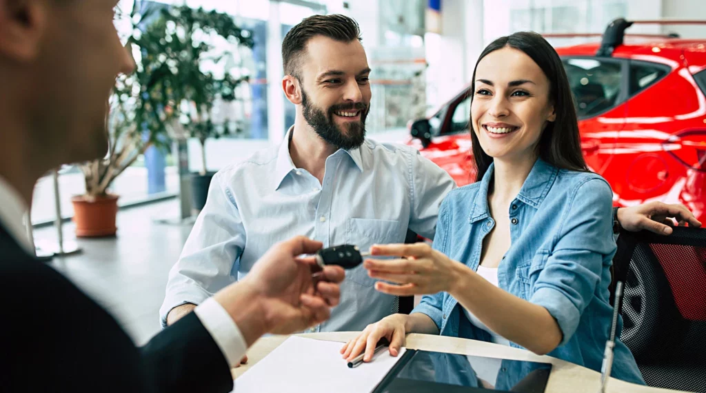 A happy couple consults with a sales person at a car dealership.