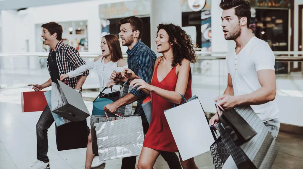 A group of friends carrying shopping bags runs excitedly through the mall together