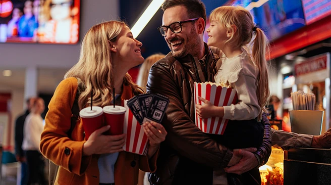 A young Caucasian family is at the movie theater, bonding as they're ready to see a movie together.