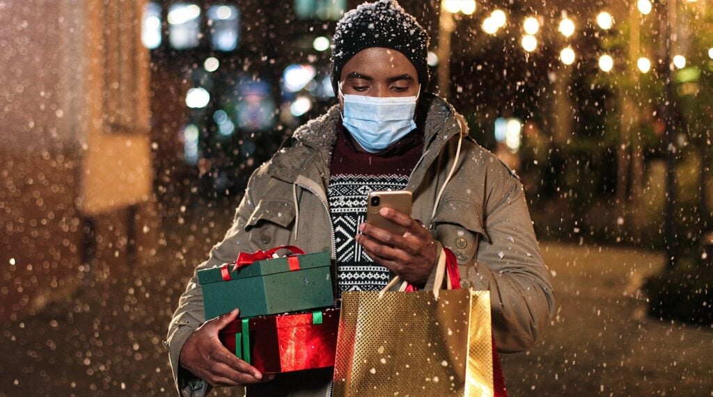 Male with shopping bags paying on smartphone with credit card while snowing