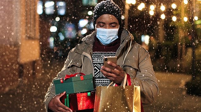 Male with shopping bags paying on smartphone with credit card while snowing